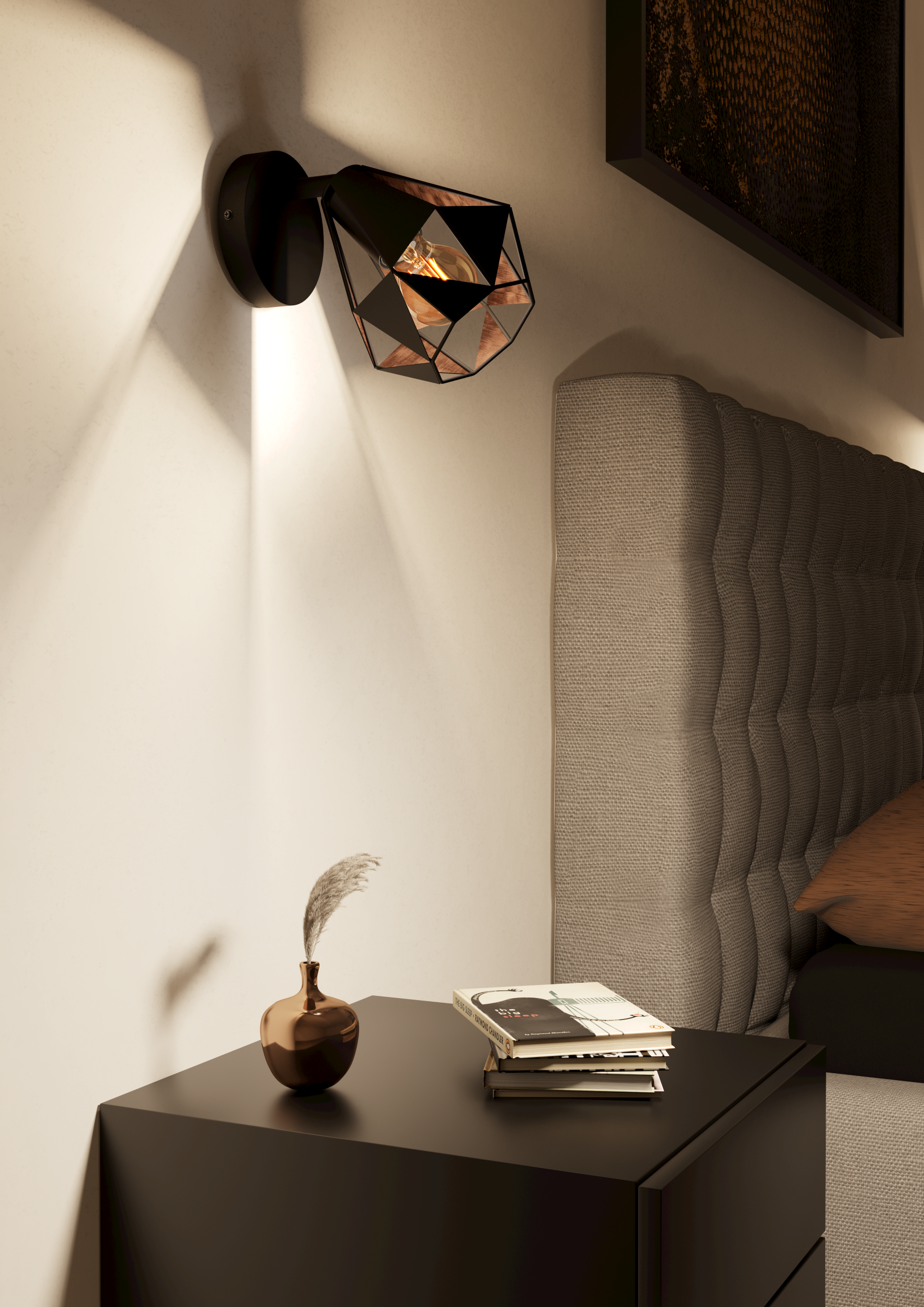 Una lámpara geométrica negra proyecta luz sobre una pared. Una mesita de noche con libros y un florero debajo.