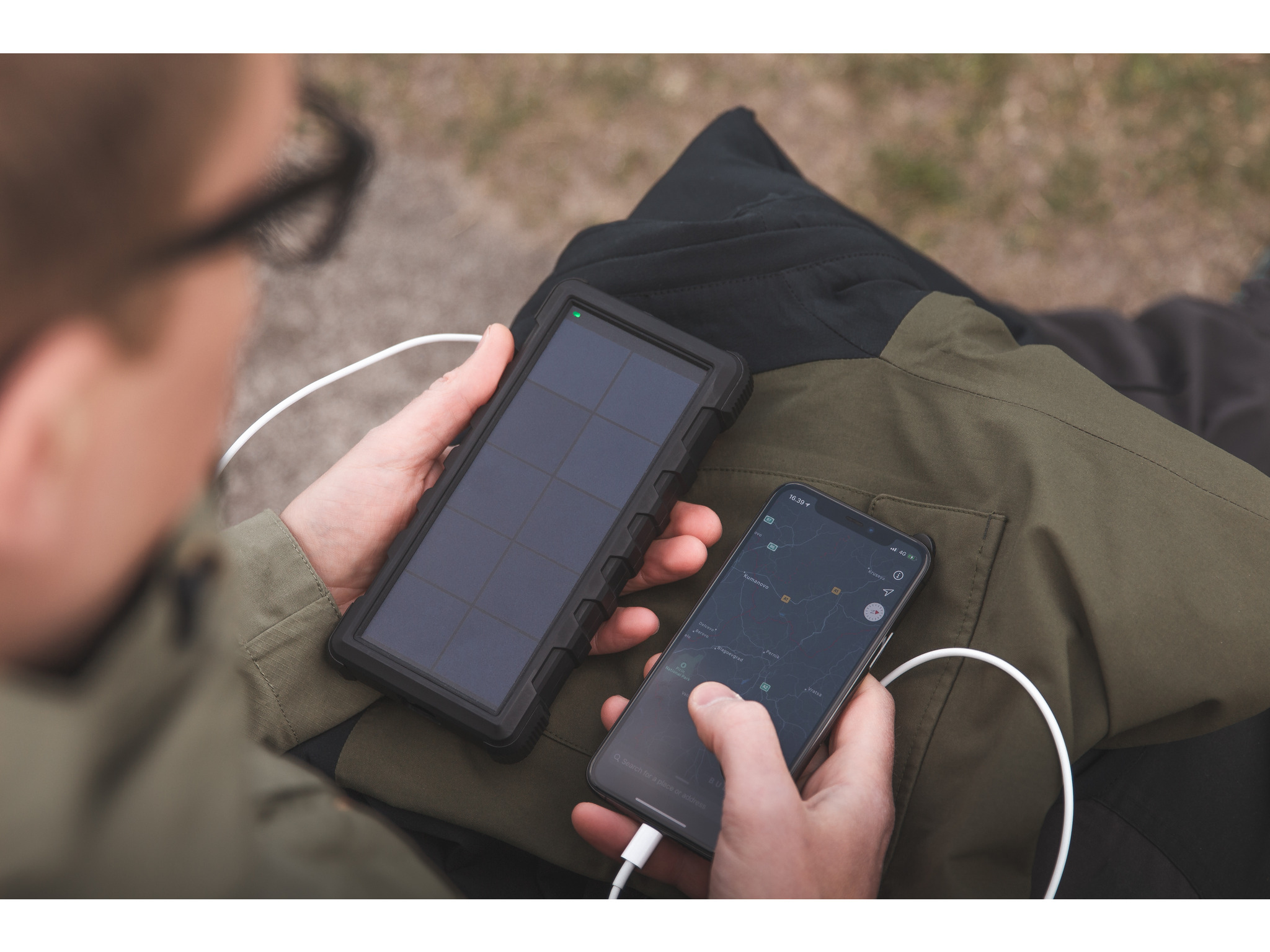 Persona che tiene in mano un caricatore solare e uno smartphone. Il telefono si sta caricando, mostrando una mappa. Persona indossa una giacca.