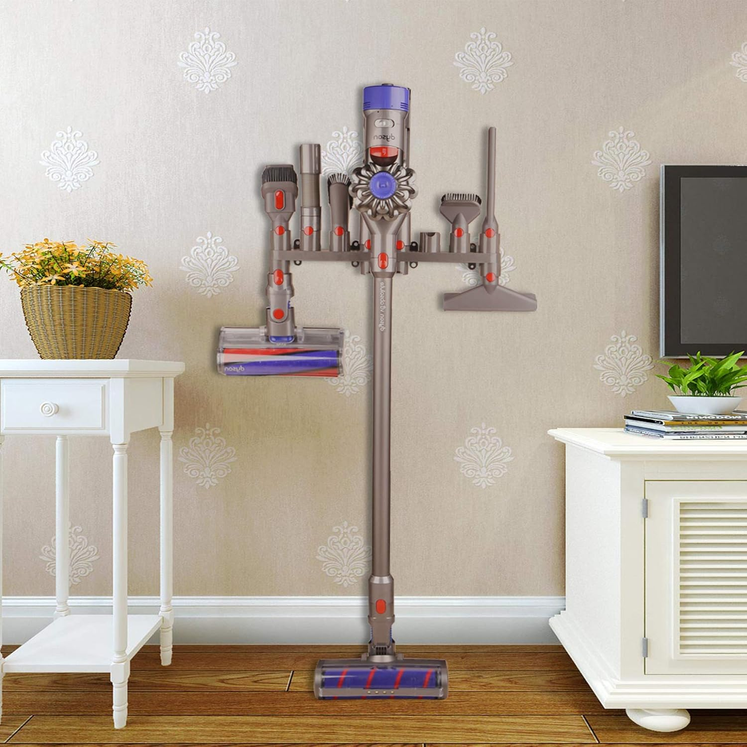 Ein Dyson-Staubsauger steht auf einem Ständer. Auf beiden Seiten befinden sich ein Tisch mit Blumen und ein Fernseher. Die Wand hat ein Muster.