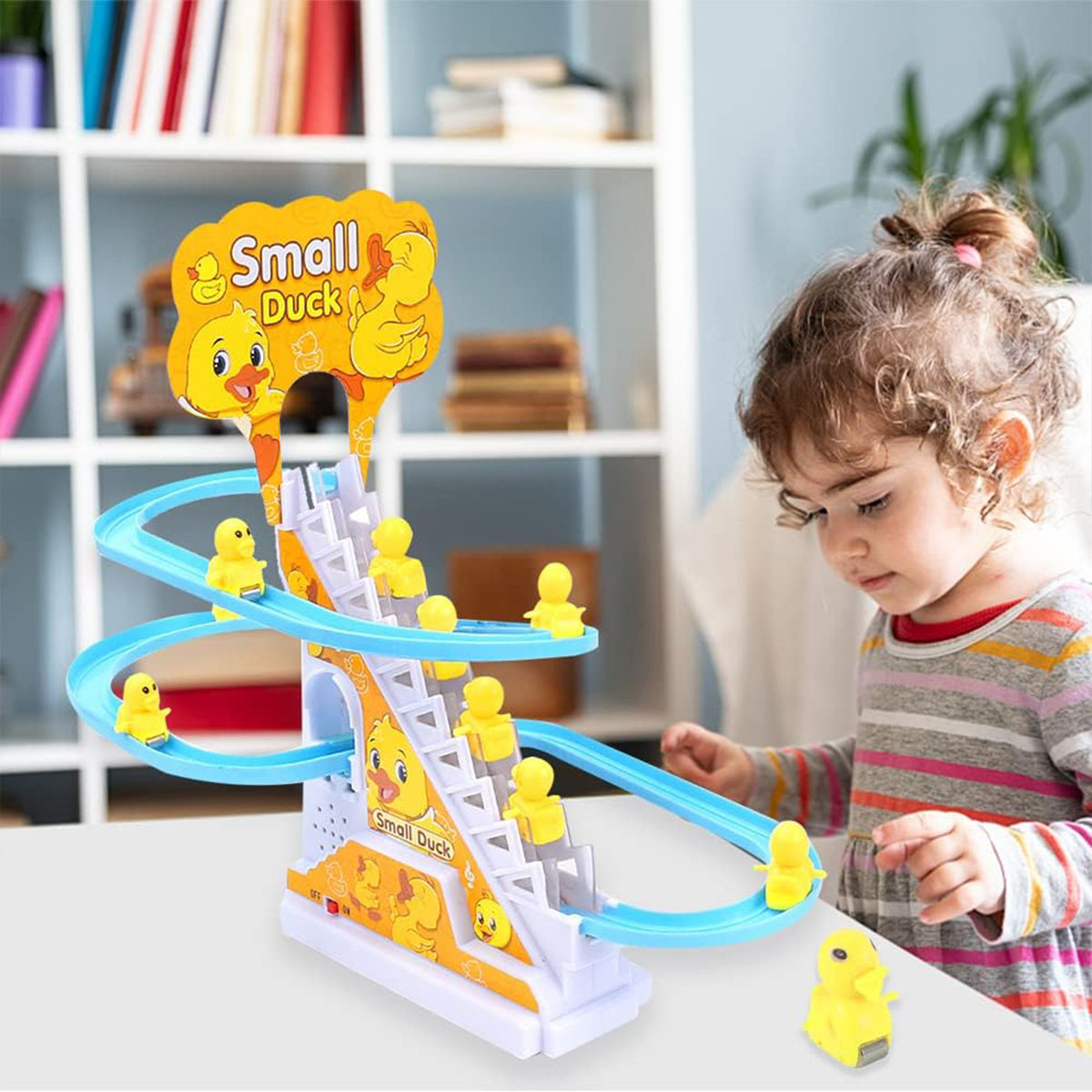 Ein Kind spielt mit einem Spielzeug-Entenrutsche. Gelbe Enten bewegen sich eine blaue Bahn hinunter. Das Spielzeug hat Treppen und die Worte 'Small Duck'.