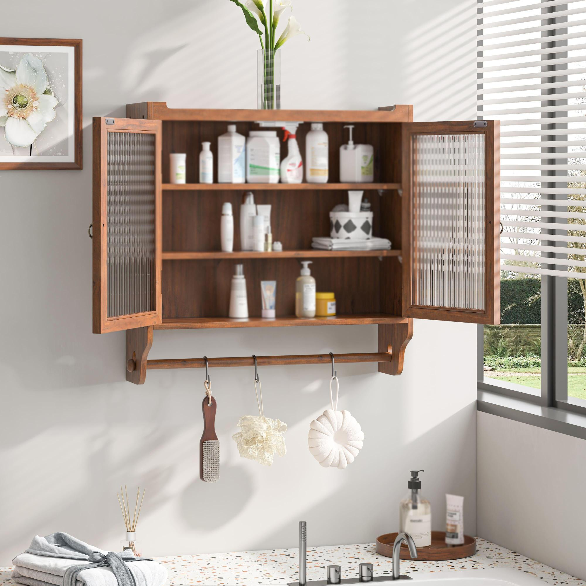Holz-Badezimmerschrank mit Glastüren. Im Inneren sind Toilettenartikel angeordnet. Darunter hält eine Handtuchstange Badeaccessoires.