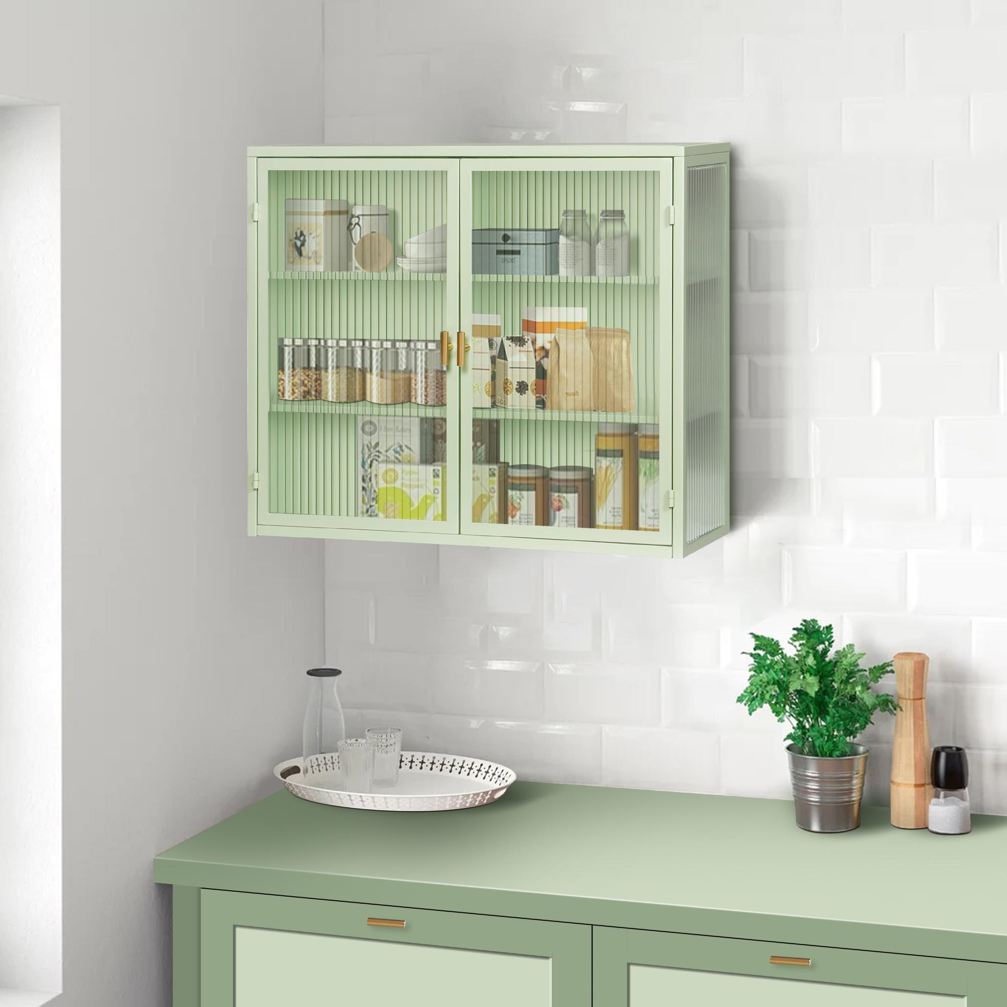 Ein mintgrüner Schrank mit Glastüren, gefüllt mit Gläsern und Verpackungen, hängt über einer grünen Theke. Eine Pflanze und Gewürze stehen auf der Theke.