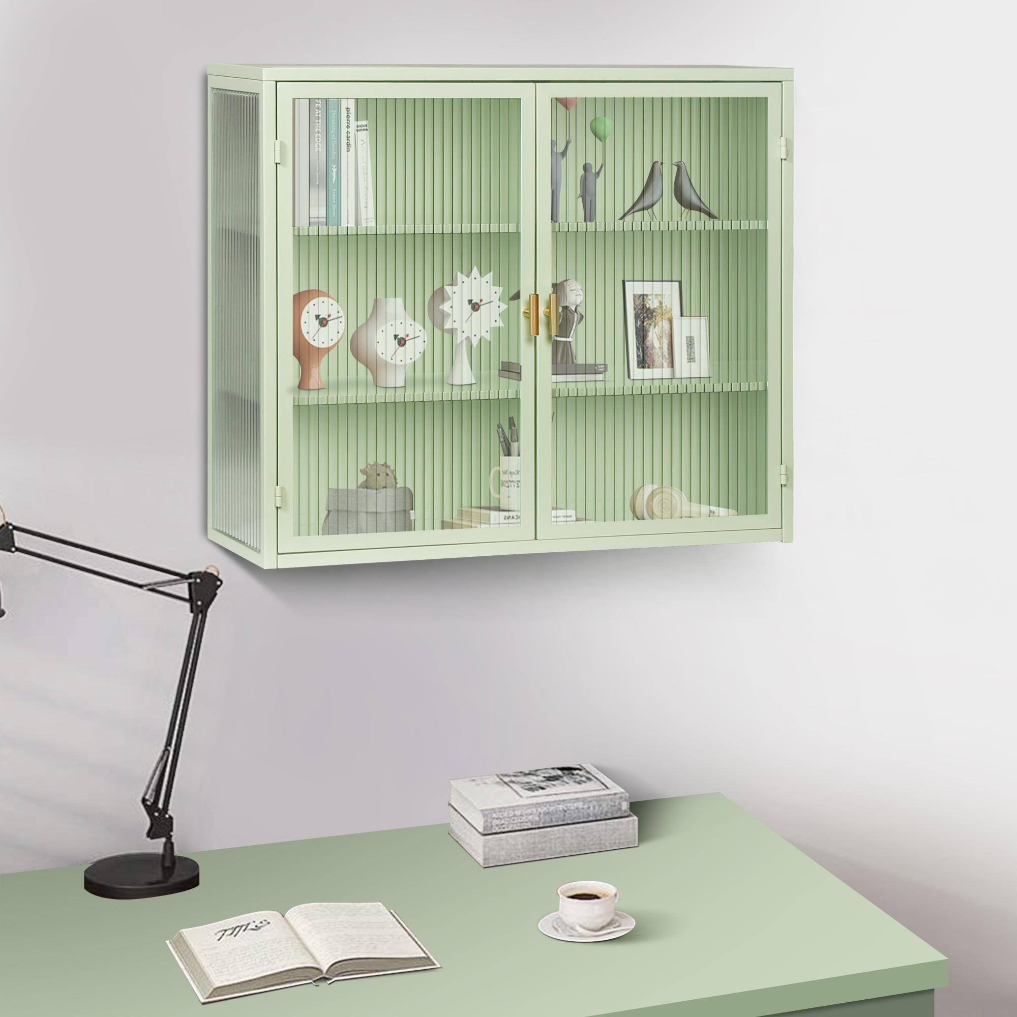 Ein mintgrüner Schrank mit Dekoration hängt über einem Schreibtisch. Auf dem Schreibtisch liegen eine Lampe und Bücher. In der Nähe steht eine Tasse Kaffee.