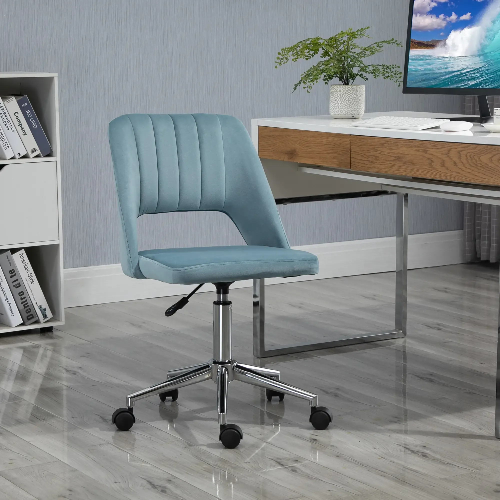 Ein tealfarbener Bürostuhl steht vor einem Schreibtisch mit Monitor und Pflanze. Links ist ein Bücherregal.