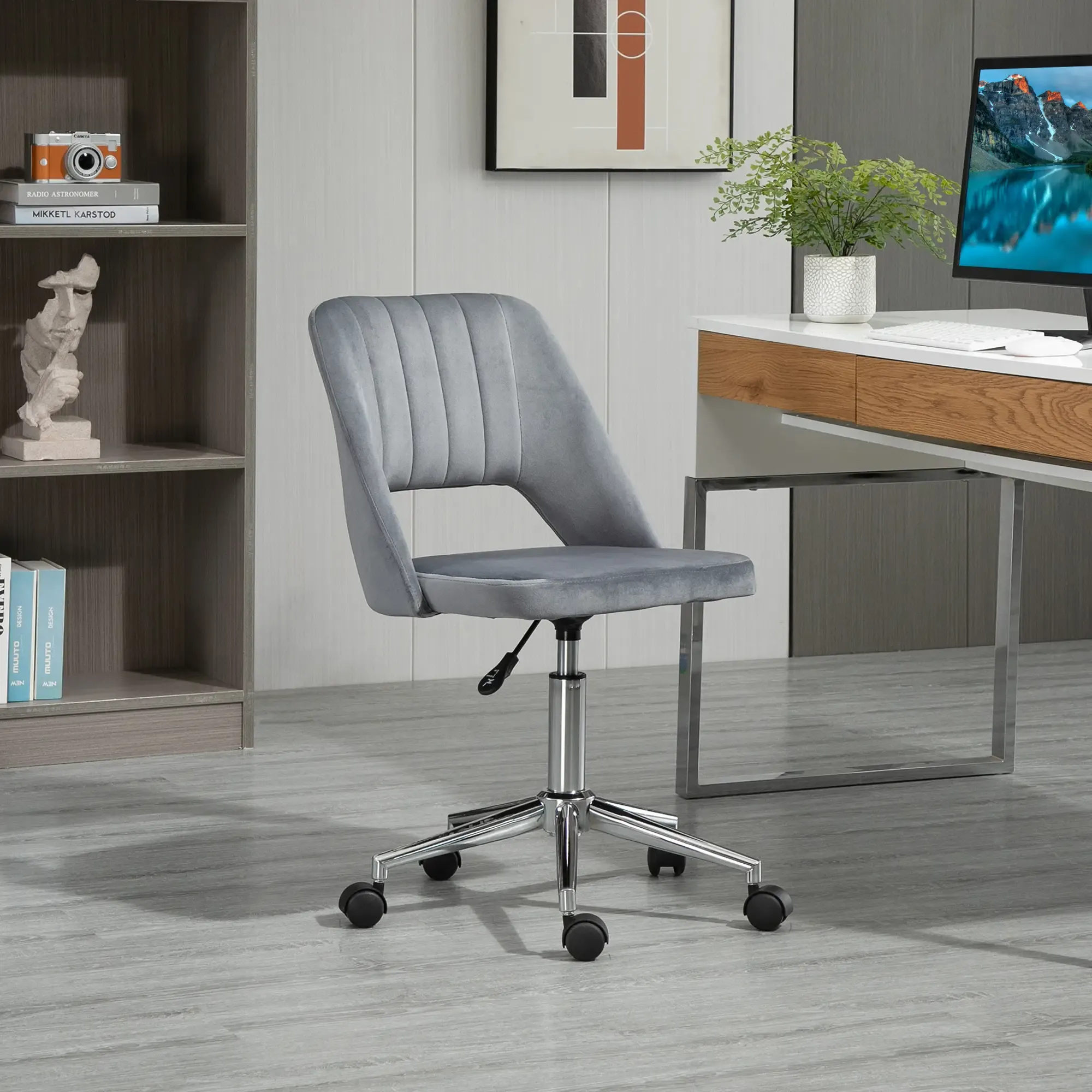 Ein grauer Samt-Bürostuhl steht in einem Raum. Ein Schreibtisch mit Computer und ein Bücherregal sind im Hintergrund.