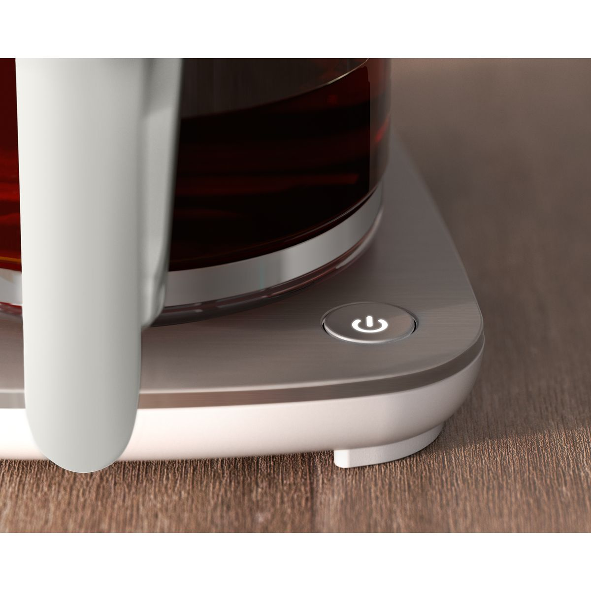 Zbliżenie szklanego czajnika z ciemnym płynem w środku. Przycisk zasilania świeci na podstawie, na drewnianej powierzchni.