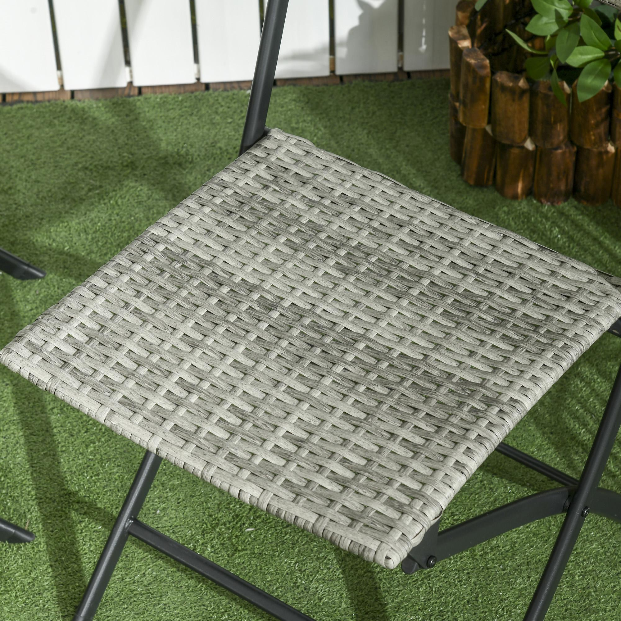 Nahaufnahme eines grauen Korbstuhls auf grünem Gras. Ein weißer Zaun und ein Holzpflanzer sind im Hintergrund.