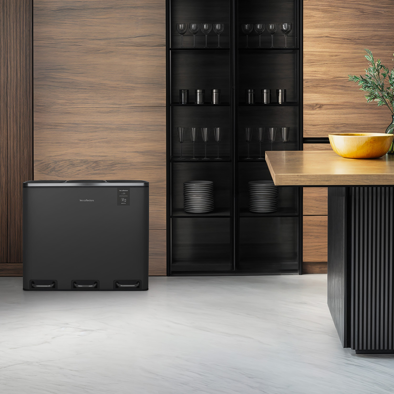 Una cucina moderna. Un bidone nero in primo piano. Un mobile in legno e un tavolo con una ciotola gialla sullo sfondo.