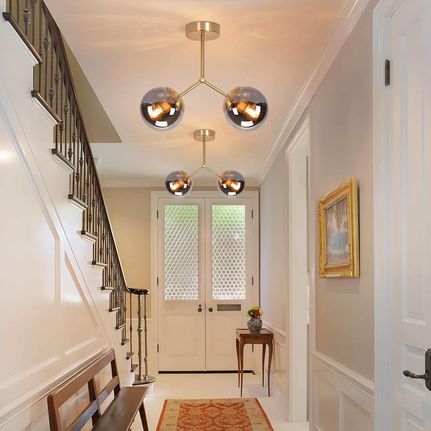 Korytarz ze schodami, ławką i stołem z kwiatami. Widoczne są dwa kuliste żyrandole i obraz na ścianie.