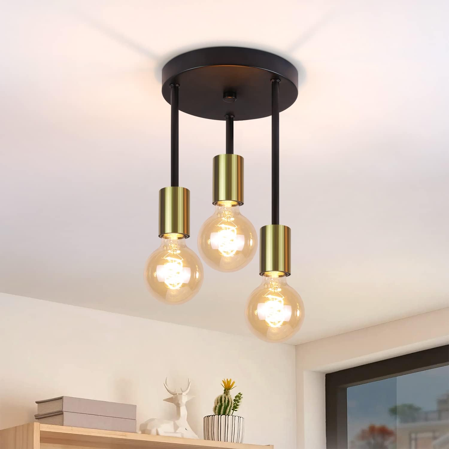 Lampa sufitowa z trzema wiszącymi żarówkami. Oprawa ma czarną podstawę ze złotymi akcentami i ciepłymi, świecącymi żarówkami.