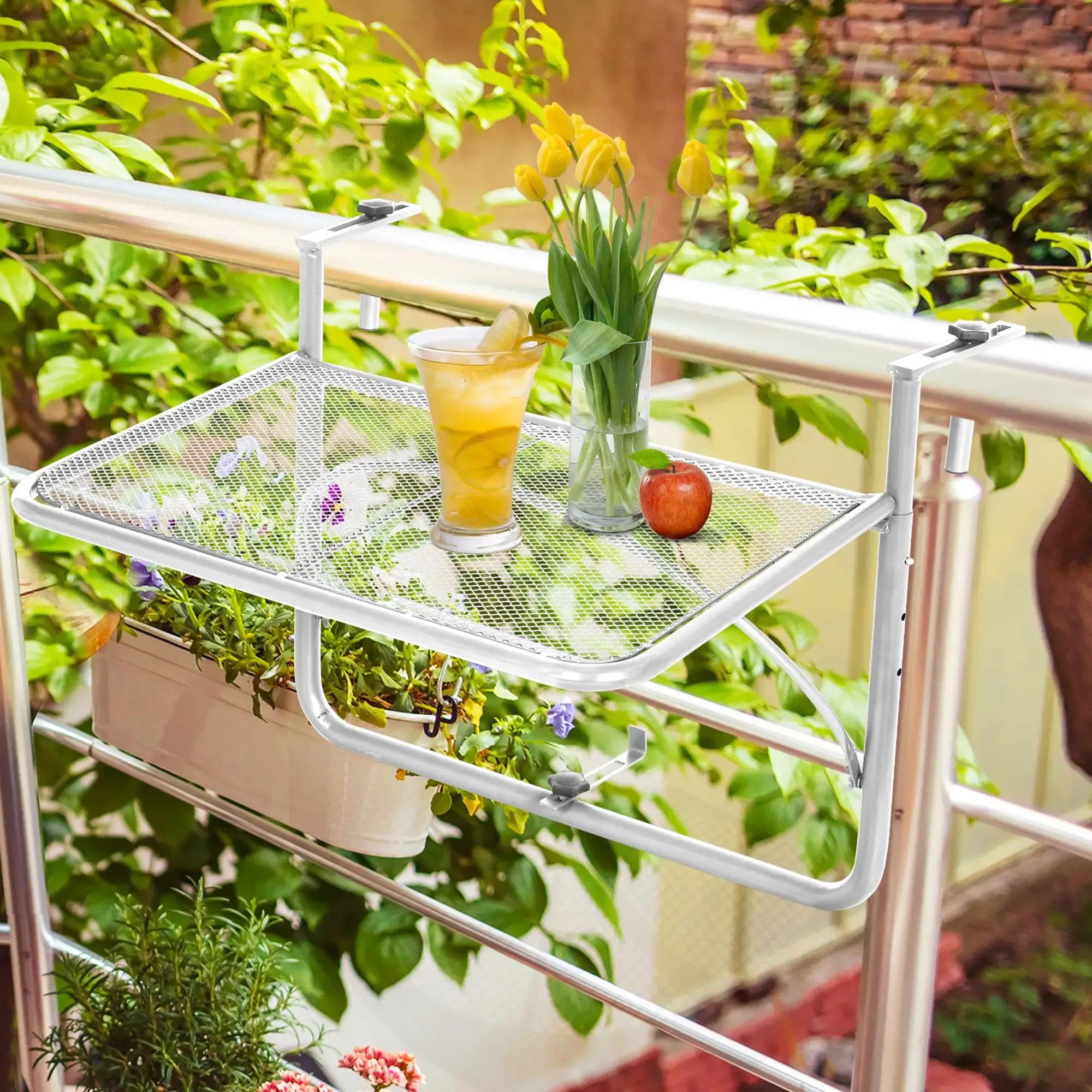 Ein Balkontisch mit Getränk, Blumen und Apfel. Grünes Laub im Hintergrund. Metallgeländer.