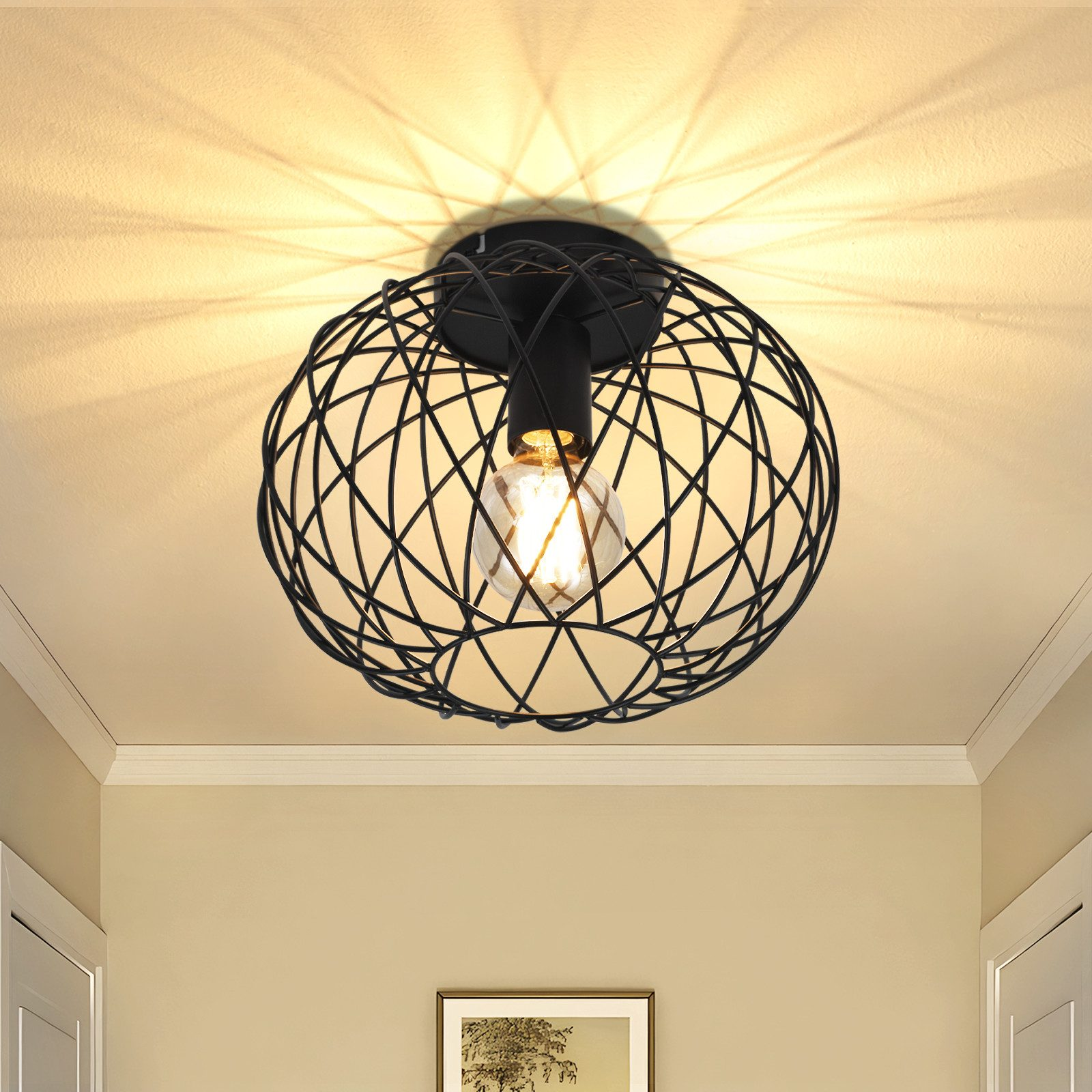Una lampada da soffitto a filo nero con una lampadina accesa è centrata. La luce proietta un motivo a stella sul soffitto.