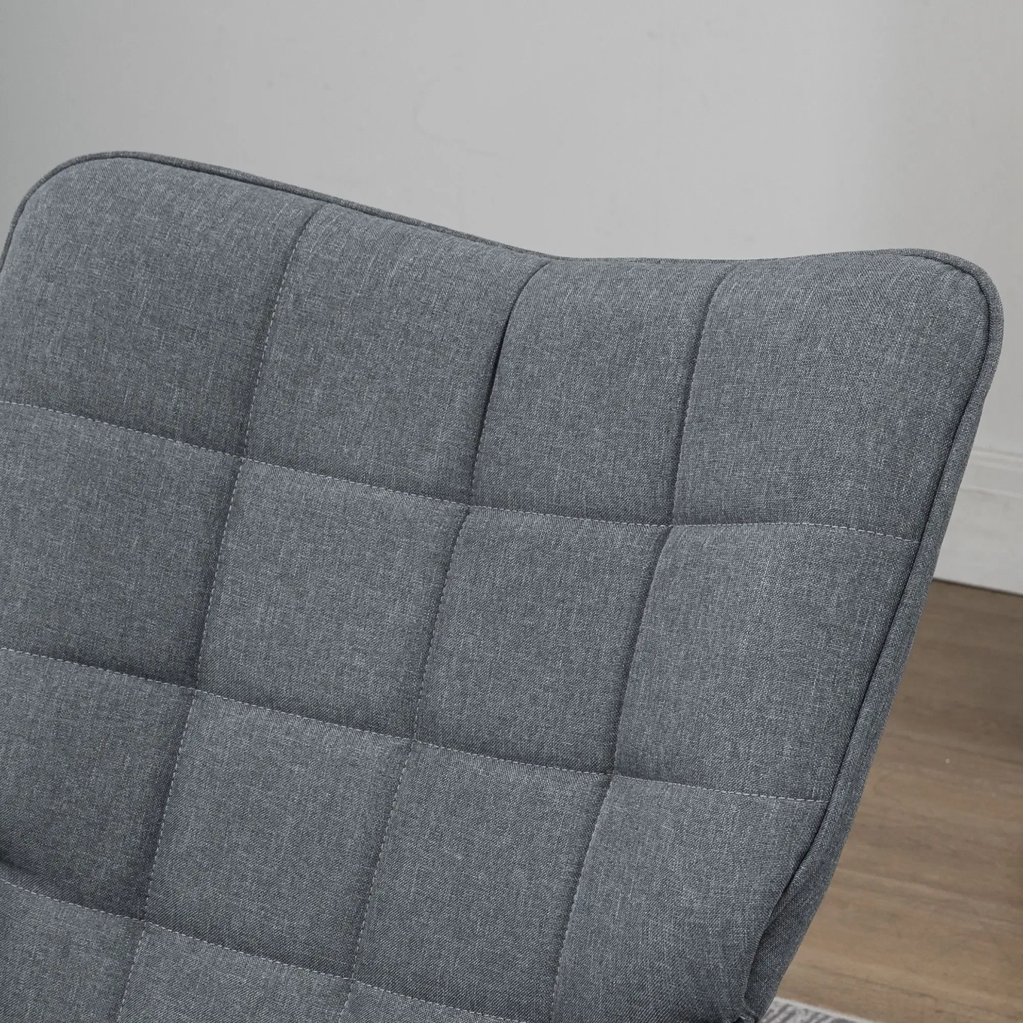 Nahaufnahme einer grauen, gepolsterten Stuhllehne. Der Stoff ist in Quadrate unterteilt. Der Hintergrund ist eine weiße Wand und Holzboden.