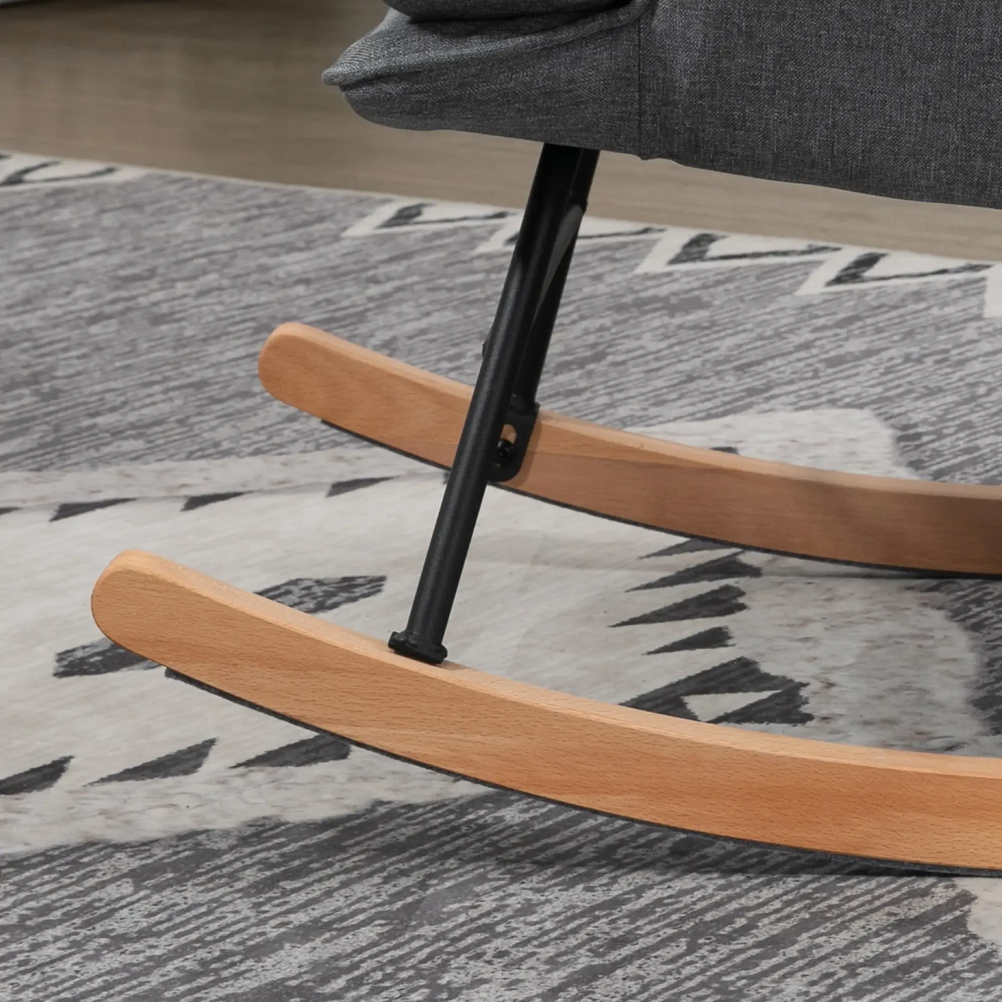 Ein grauer Schaukelstuhl mit Holzschaukeln und einer schwarzen Stütze. Der Stuhl steht auf einem gemusterten Teppich.