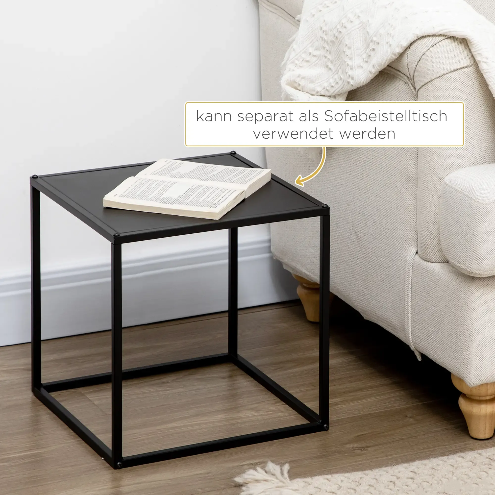 Ein schwarzer Beistelltisch mit einem Buch darauf, neben einem Sofa. Der Tisch hat eine quadratische Platte.