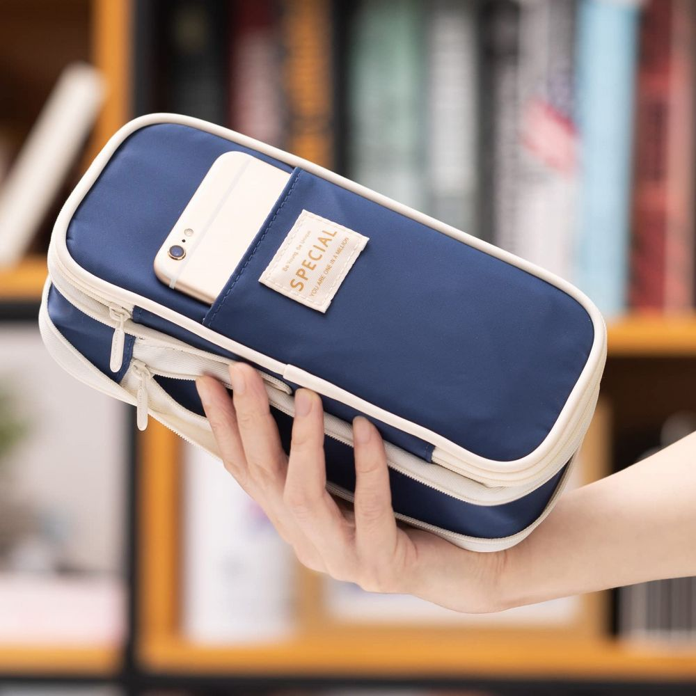 Eine Hand hält ein blaues Federmäppchen mit einem Telefon in der Tasche. Es hat einen Reißverschluss und ein "special"-Etikett. Bücher sind im unscharfen Hintergrund.