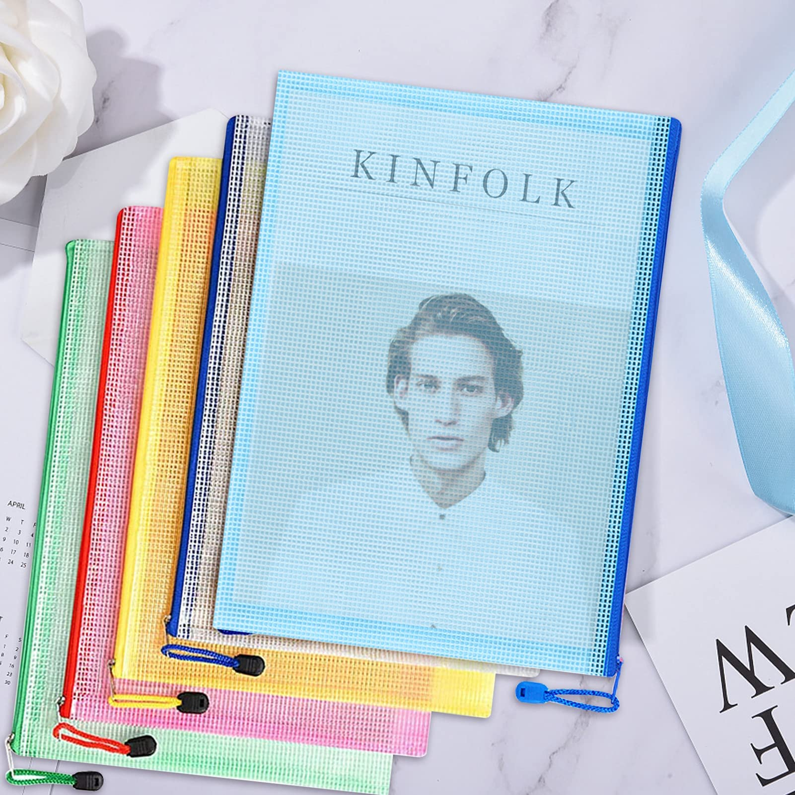Ein Stapel bunter Dokumentenhalter aus Mesh, der oberste mit einem Männergesicht und 'KINFOLK'.