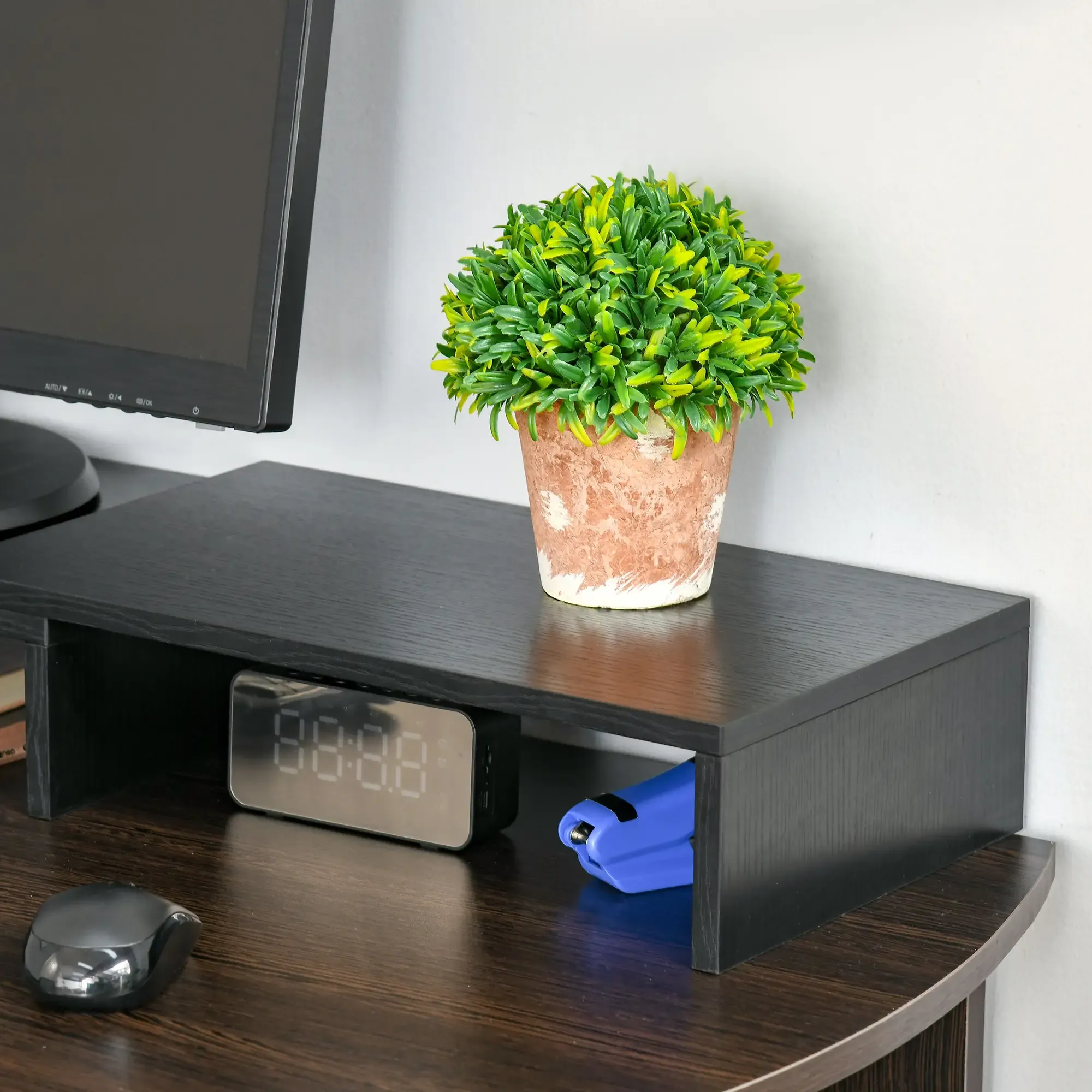 Ein Schreibtisch mit Monitor, Pflanze, Uhr und Tacker. Der Schreibtisch ist aus dunklem Holz.