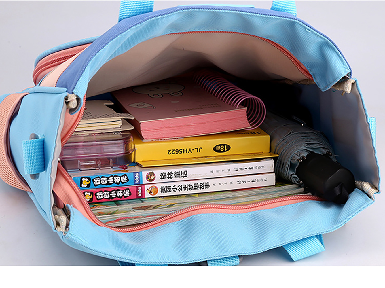 Offener blau-rosa Rucksack gefüllt mit Büchern, einem Notizbuch und einem Regenschirm. Der Rucksack hat blaue Träger und einen Reißverschluss.