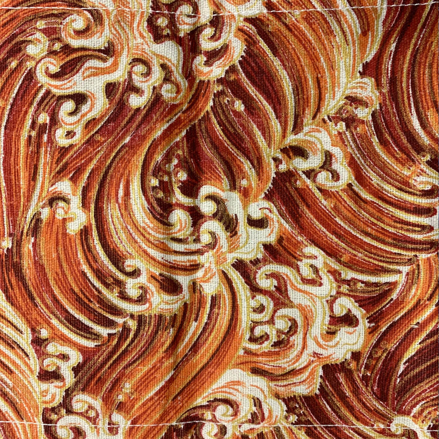 Nahaufnahme eines Stoffes mit wirbelnden Mustern in Orange-, Rot- und Cremetönen. Das Design ähnelt stilisierten Wellen oder Flammen.