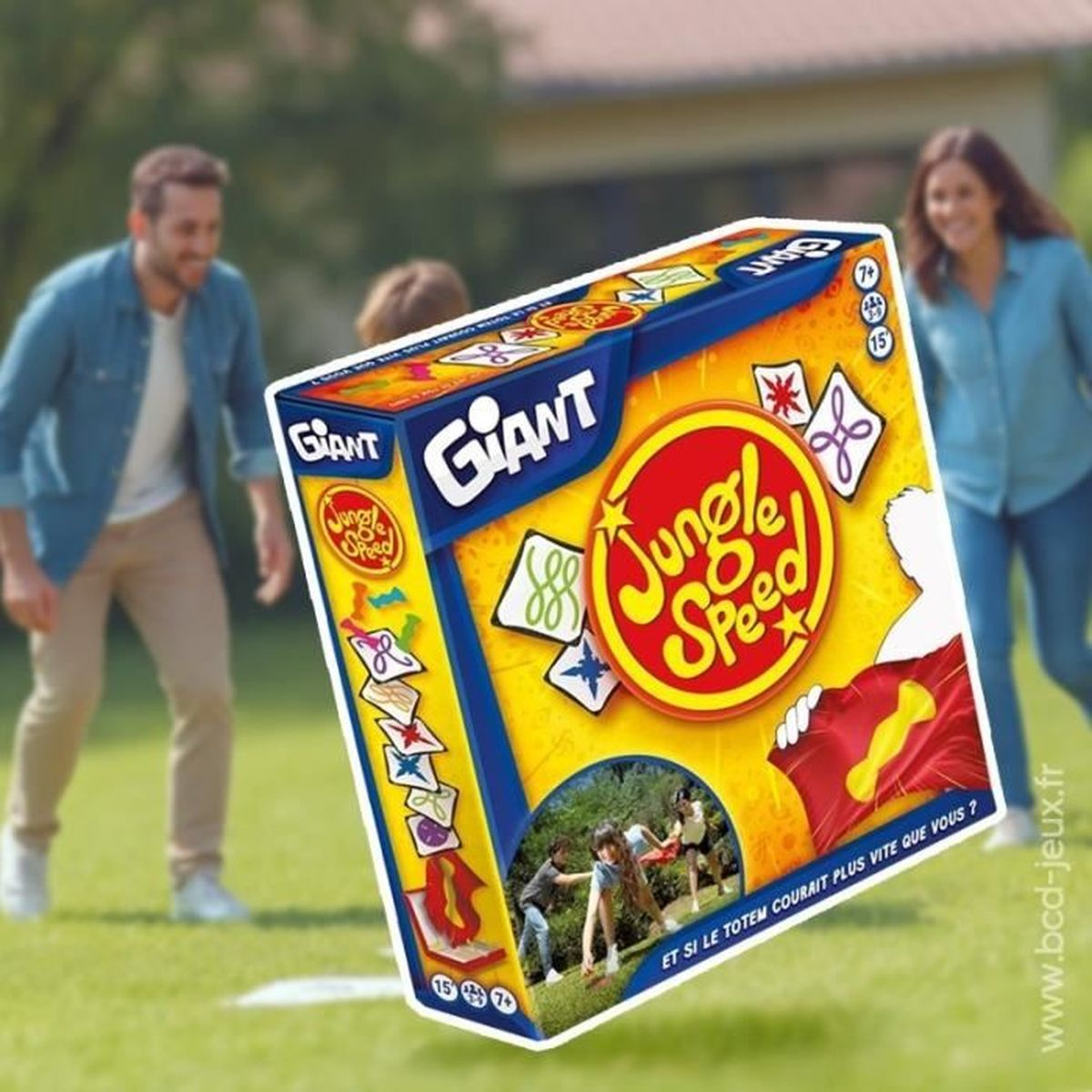 Eine Familie spielt draußen mit einer Jungle Speed-Spielbox. Die Box ist gelb, mit einem roten Kreis und Text. Menschen sind im Hintergrund.