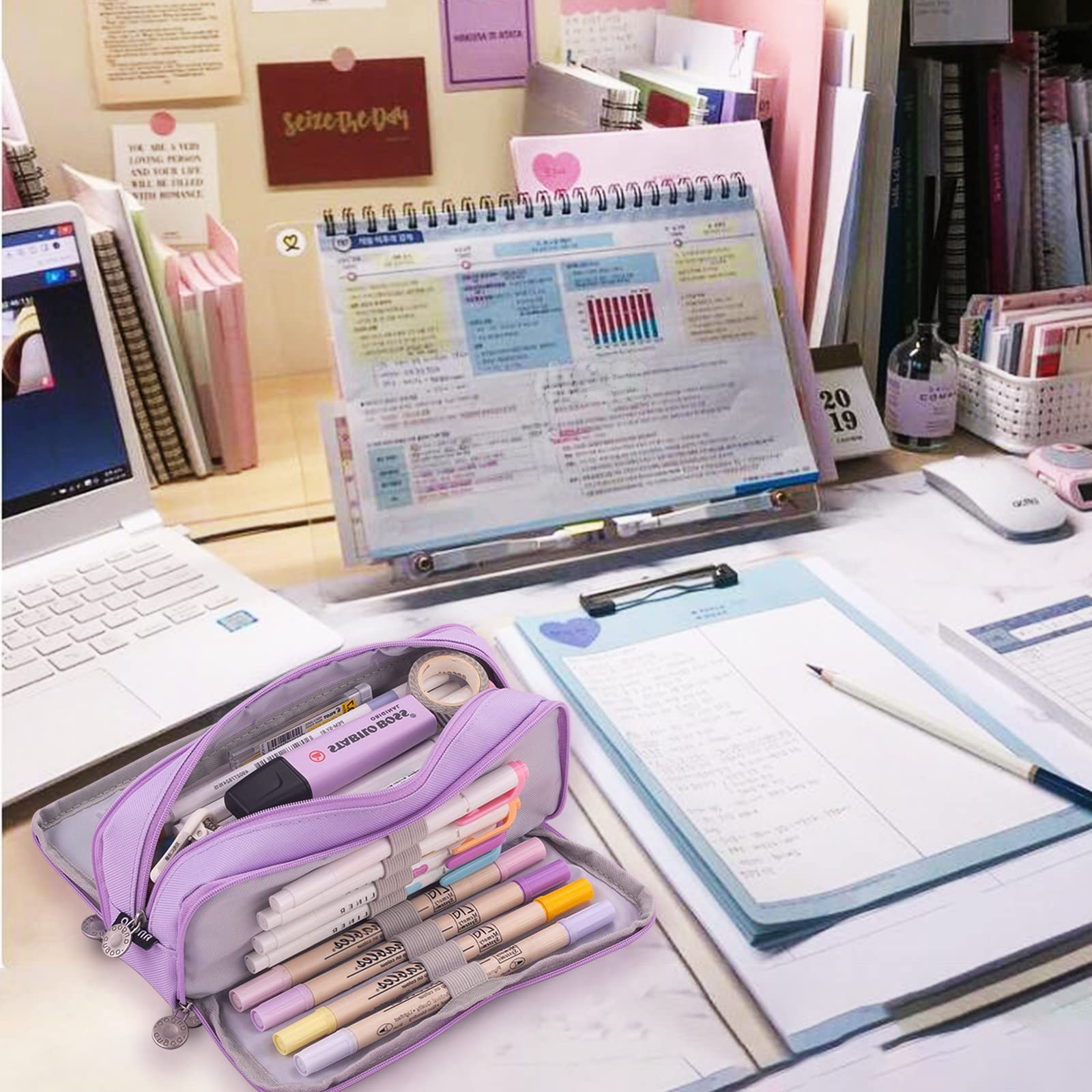 Ein Schreibtisch mit Laptop, Kalender, Stiften und einem lila Federmäppchen. Papiere und Notizen liegen auf dem Schreibtisch verstreut.