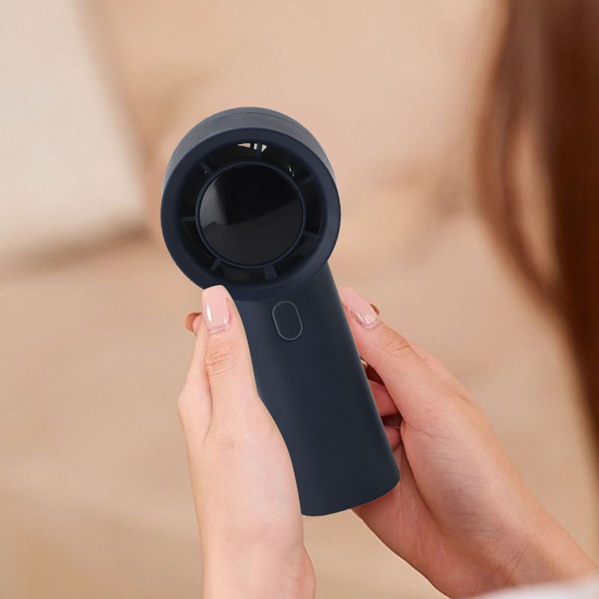 Eine Person hält einen kleinen, dunkelblauen Handventilator. Der Ventilator ist zylindrisch mit einer schwarzen Öffnung. Der Hintergrund ist verschwommen.