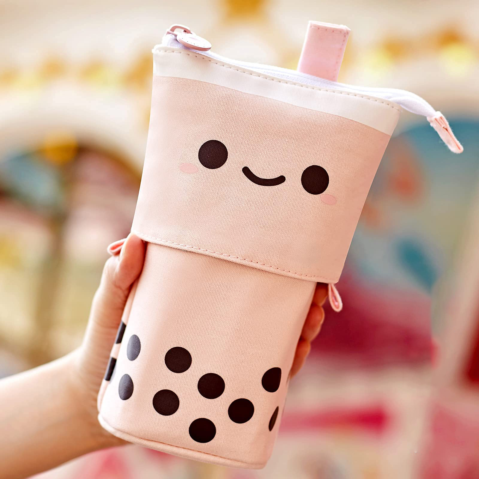 Ein rosa Boba-Tee-Federmäppchen mit einem lächelnden Gesicht, gehalten von einer Hand.