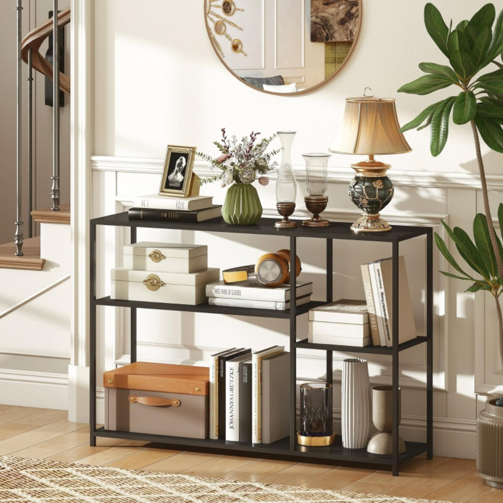 Ein schwarzes Metallregal mit Büchern, Kisten, einer Lampe und Dekorationen. Im Hintergrund ist eine Treppe zu sehen.