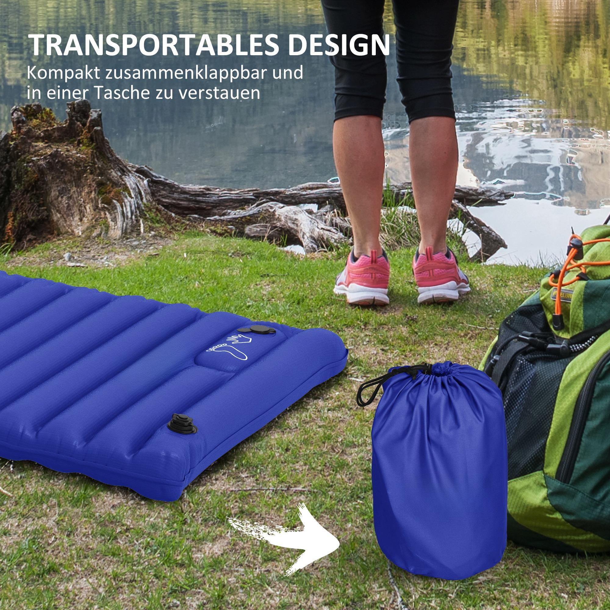 Eine blaue aufblasbare Matte, eine blaue Tasche und ein Rucksack auf Gras. Eine Person steht im Hintergrund. See im Hintergrund.