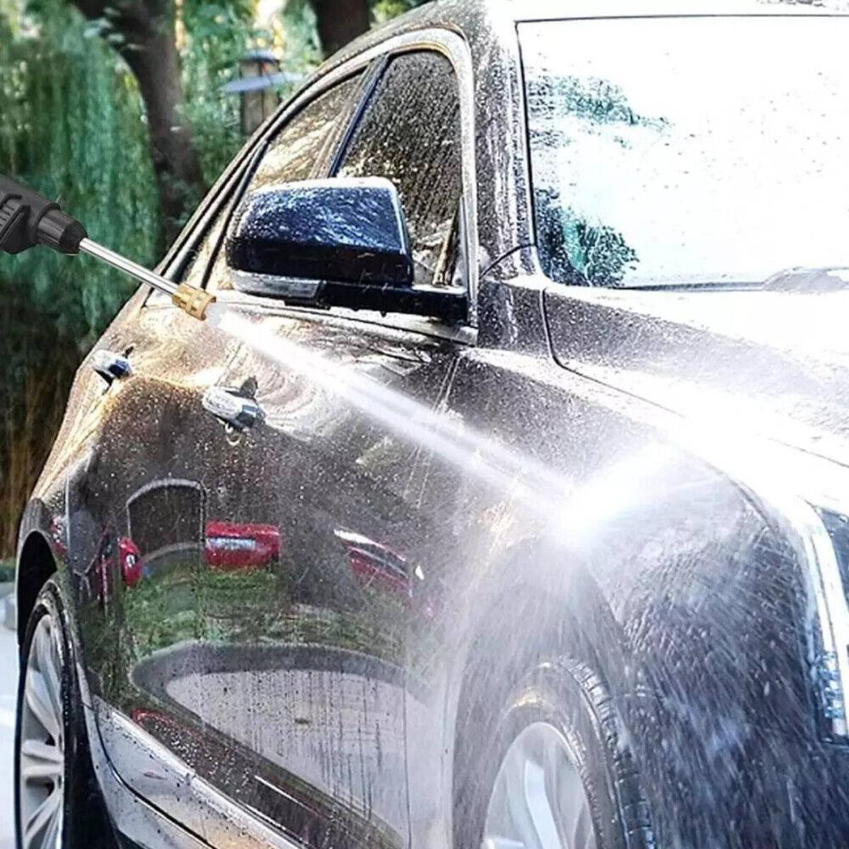 Ein schwarzes Auto wird mit einem Hochdruckreiniger gewaschen. Wasser spritzt über die Seite des Autos. Der Hintergrund zeigt grüne Bäume.