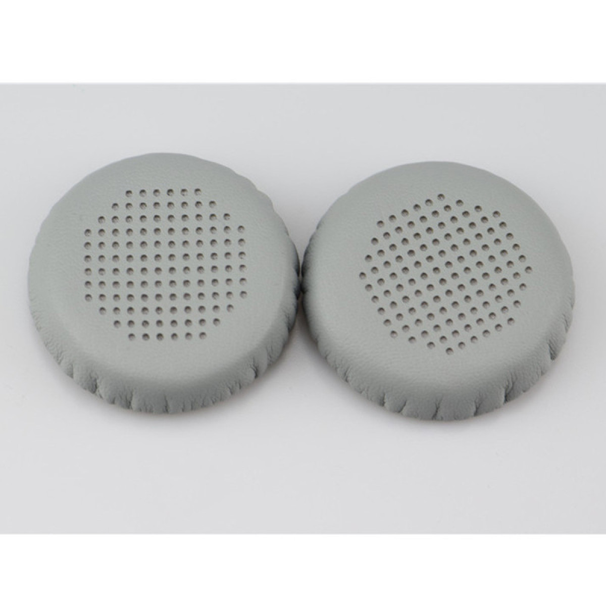 Due cuscinetti auricolari grigi per cuffie con centri perforati su una superficie bianca. I cuscinetti sono rotondi e leggermente strutturati.