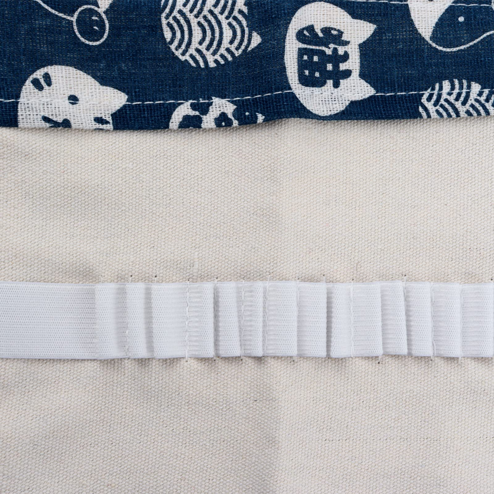 Nahaufnahme von Stoff. Blauer Stoff mit weißen Katzenmustern, weißes Gummiband auf beigem Stoff.