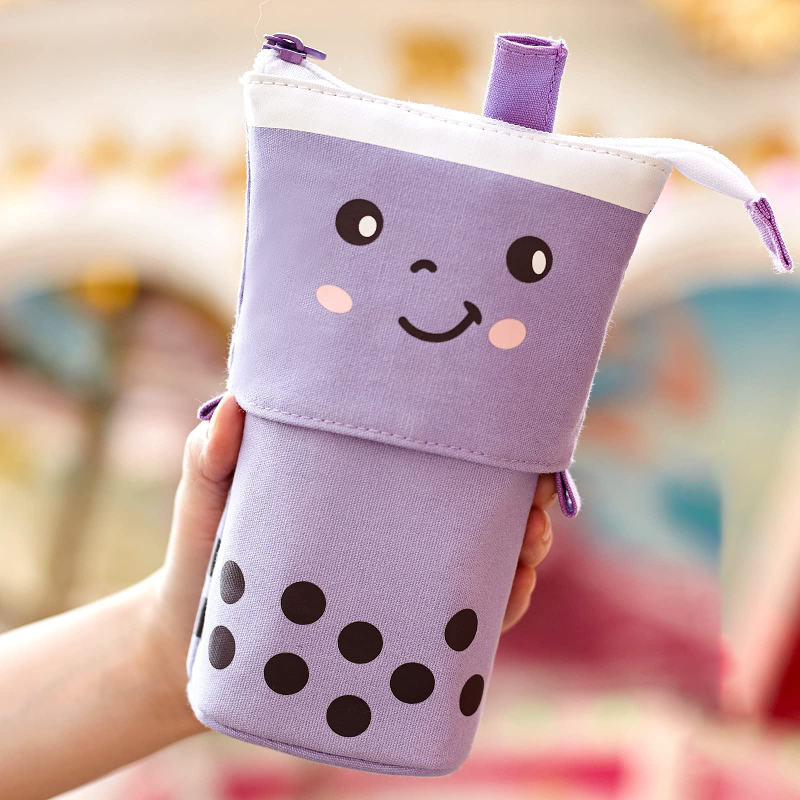 Eine Hand hält ein lila Federmäppchen in Form einer Boba-Tee-Tasse mit einem Smiley-Gesicht. Schwarze Punkte befinden sich auf der Tasse.