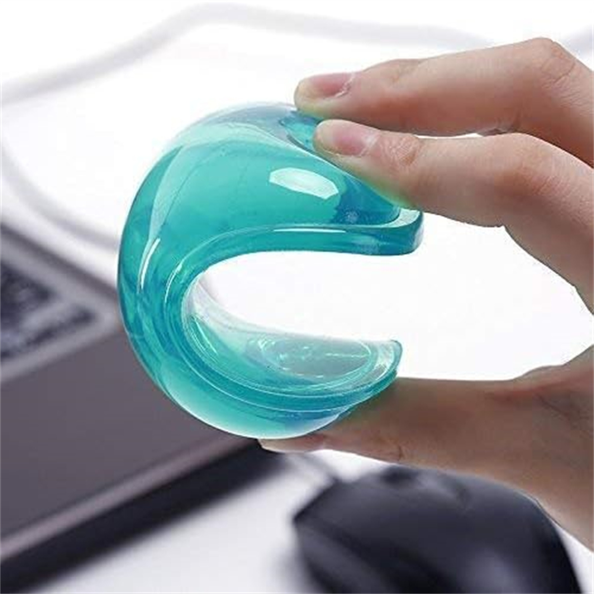 Eine Hand hält eine klare, türkisfarbene Gelform. Eine Computermaus und ein Teil eines Laptops sind im unscharfen Hintergrund.