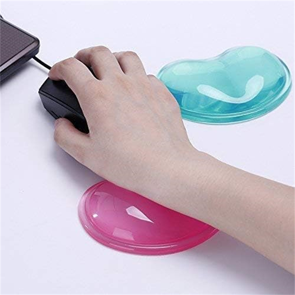 Eine Hand benutzt eine schwarze Maus auf weißem Untergrund, im Hintergrund ein rosa und ein blaues Gel-Handgelenk.