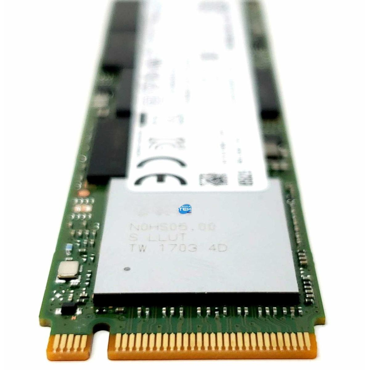 Eine Computerkomponente, eine M.2-SSD, liegt auf weißem Grund. Sie hat eine grüne Leiterplatte, goldene Anschlüsse und ein silbernes Etikett.