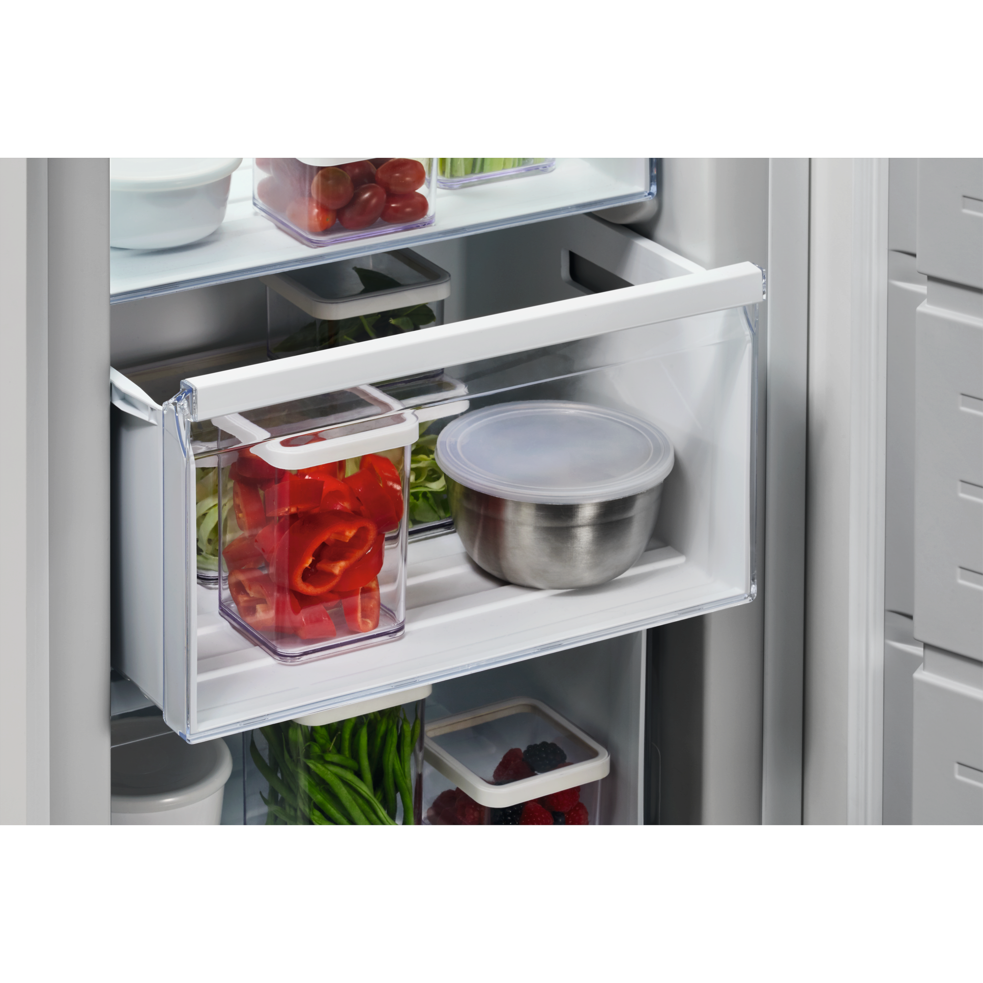 Interior de refrigerador con verduras y frutas en recipientes transparentes, tazón de acero inoxidable, en estantes. Pimientos rojos, tomates y bayas.