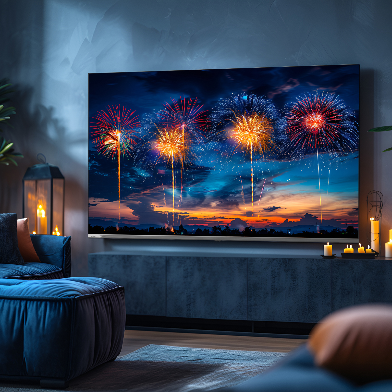 Une télévision affiche un feu d'artifice au coucher du soleil. Un canapé bleu, des bougies et une lanterne dans la pièce.
