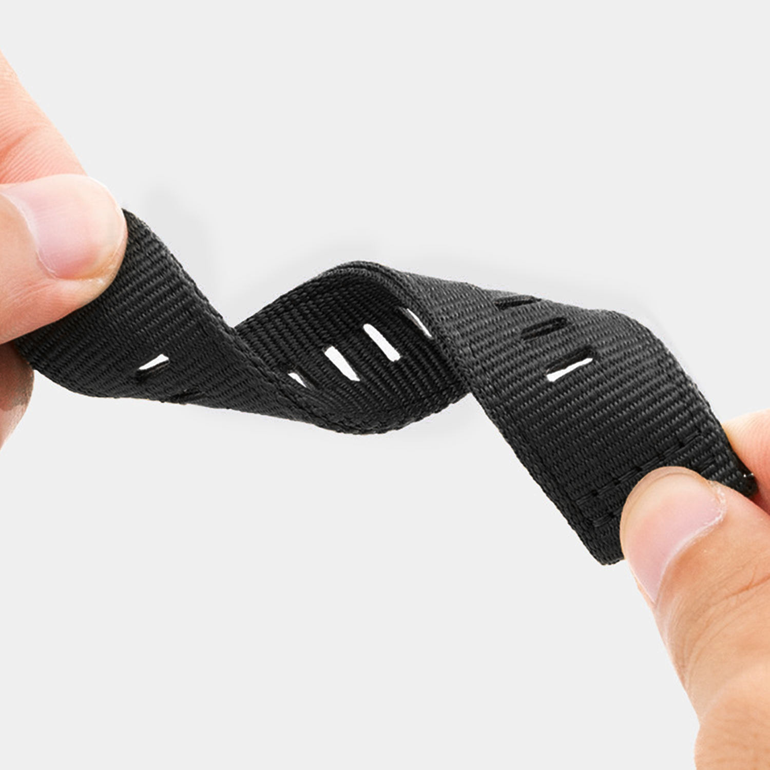 Dłonie trzymają czarny pasek z otworami. Pasek jest wygięty na jasnym tle.