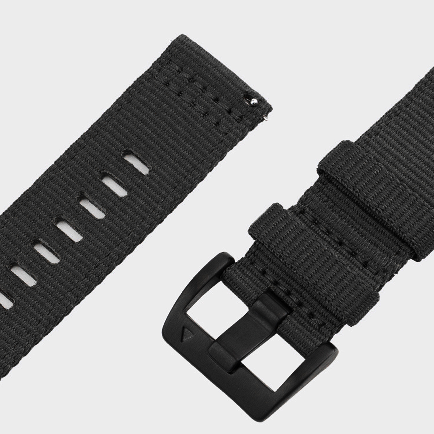 Czarny pasek do zegarka z klamrą i otworami, odłączony. Pasek wykonany jest z tkanego materiału. Tło jest neutralnie szare.