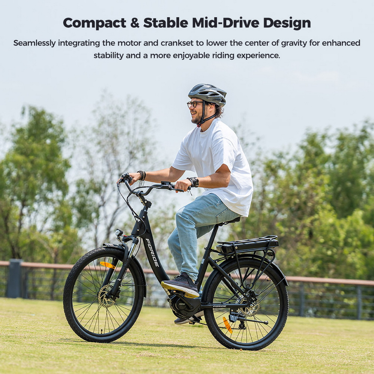 Mężczyzna jedzie czarnym rowerem elektrycznym po trawie. Ma na sobie kask, białą koszulę i dżinsy. W tle drzewa.