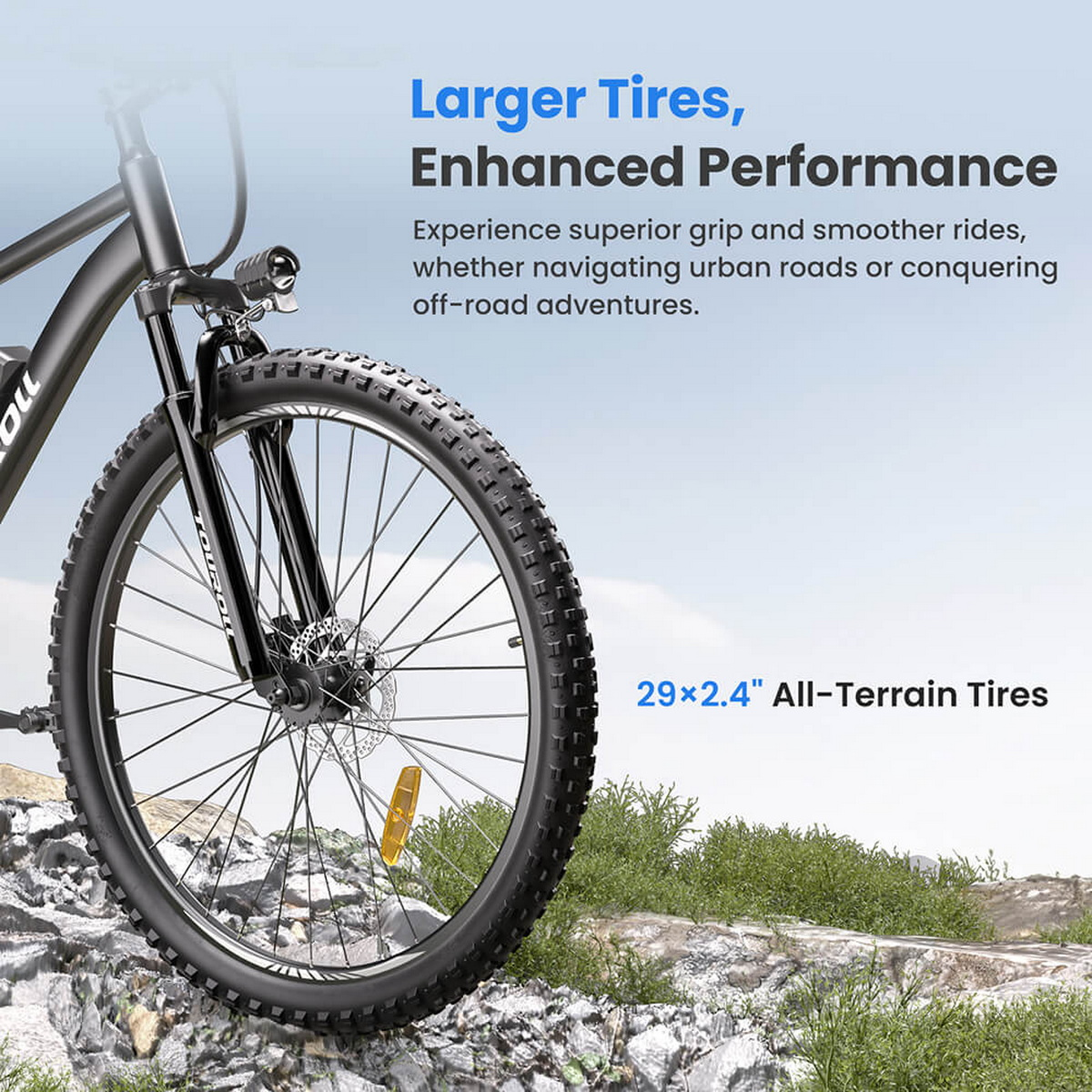 Czarna opona do roweru górskiego, przednie koło w centrum. Tekst reklamuje większe opony dla lepszej wydajności. Tło to skalisty teren.