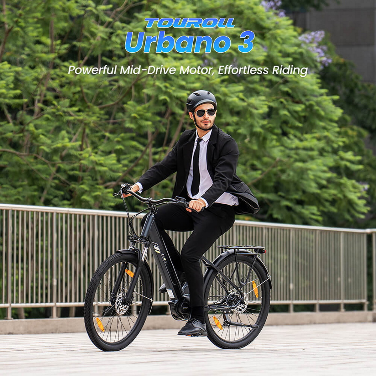 Mężczyzna w garniturze jedzie na czarnym rowerze. Rower ma pomarańczowe odblaski. W tle zielone drzewa. Tekst mówi Urbano 3.