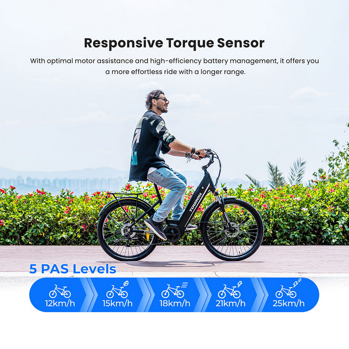 Mężczyzna jedzie czarnym rowerem elektrycznym po ścieżce. Znajduje się przed zielonymi krzewami i czerwonymi kwiatami. Obraz promuje cechy roweru.