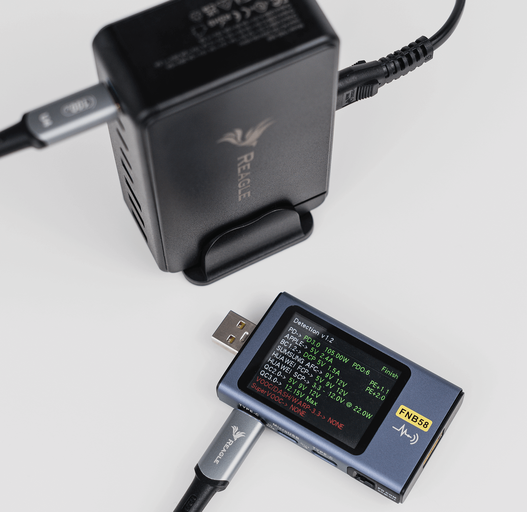 Czarna ładowarka z podłączonym kablem i niebieskie urządzenie wyświetlające informacje o napięciu i prądzie. Białe tło.