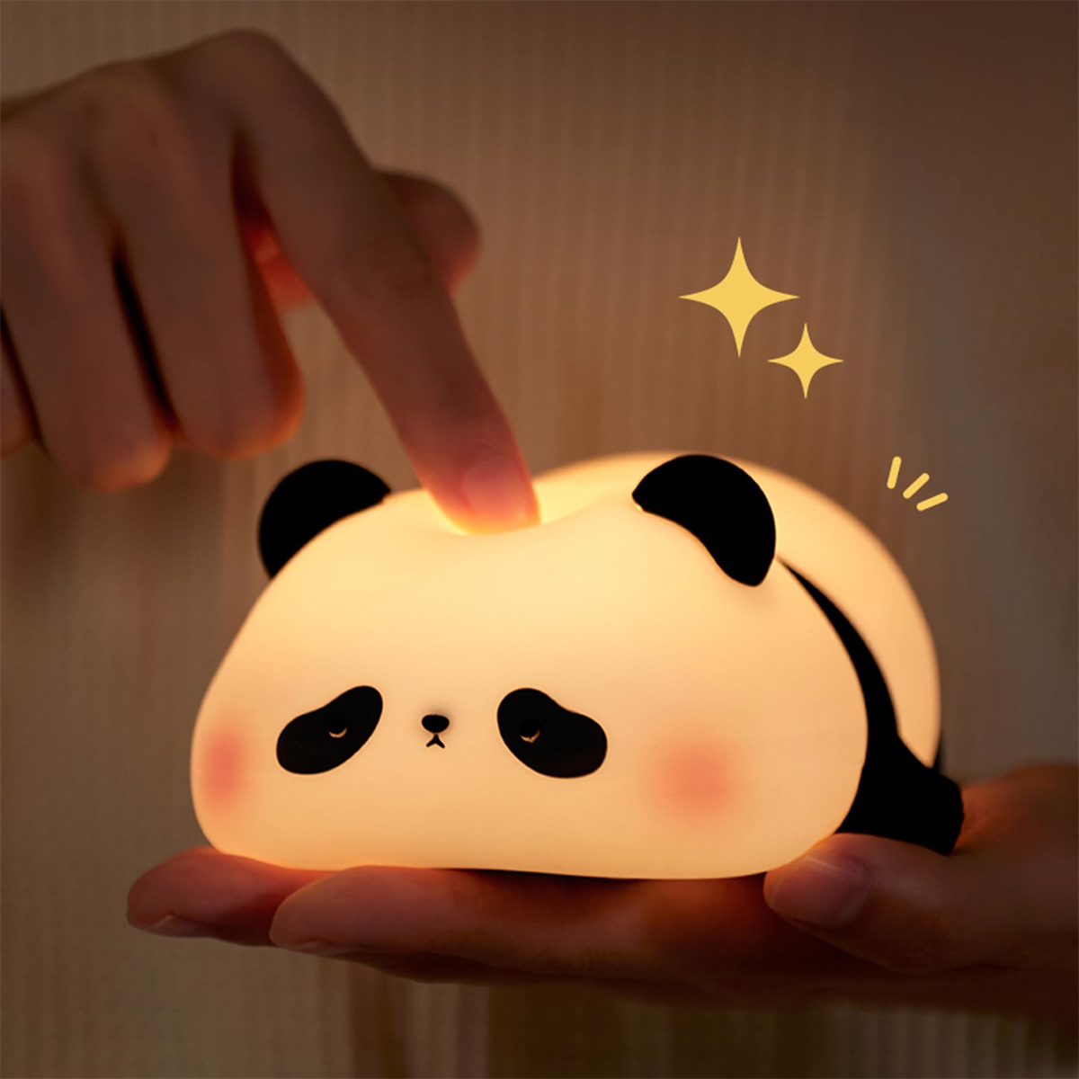 Eine Hand berührt ein panda-förmiges Nachtlicht. Das Licht ist weiß mit schwarzen Ohren und Augen. Zwei gelbe Sterne sind über dem Licht gezeichnet.