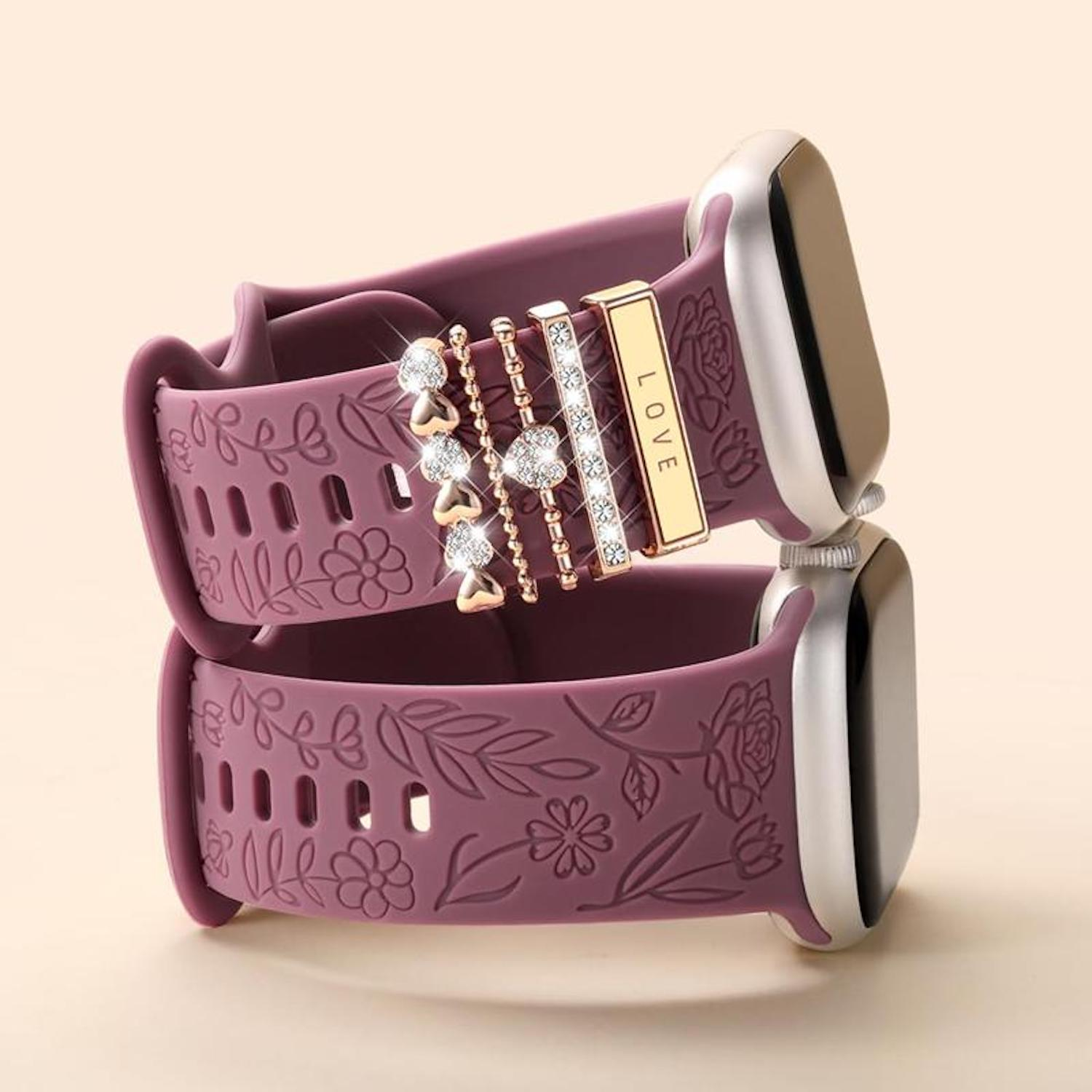 Zwei gestapelte lila Uhrenarmbänder mit floralen Mustern. Ein Band hat einen Anhänger mit dem Wort LIEBE. Die Zifferblätter sind silbern.