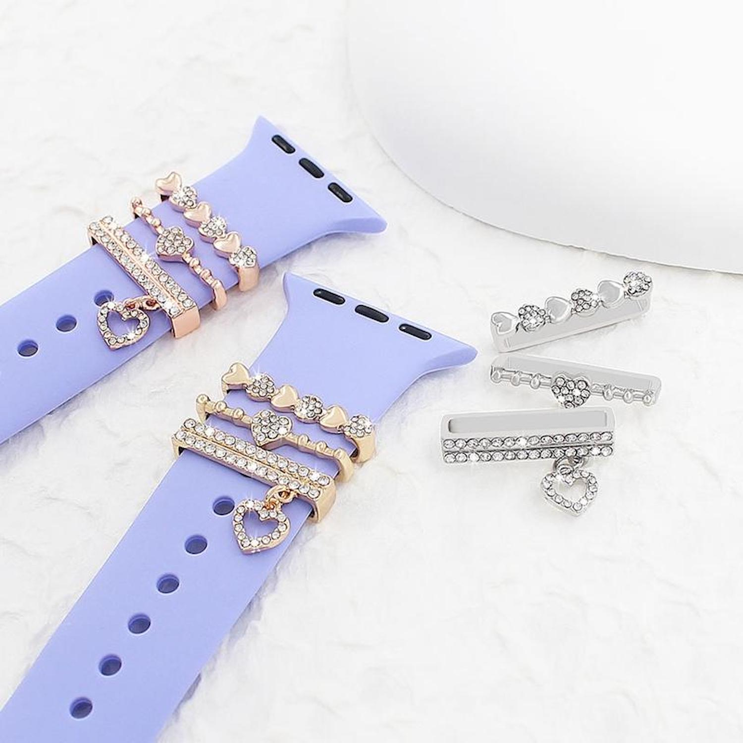 Zwei lila Uhrenarmbänder mit dekorativen goldenen und silbernen Herzanhängern. Silberne und goldene Anhänger sind auch separat platziert.