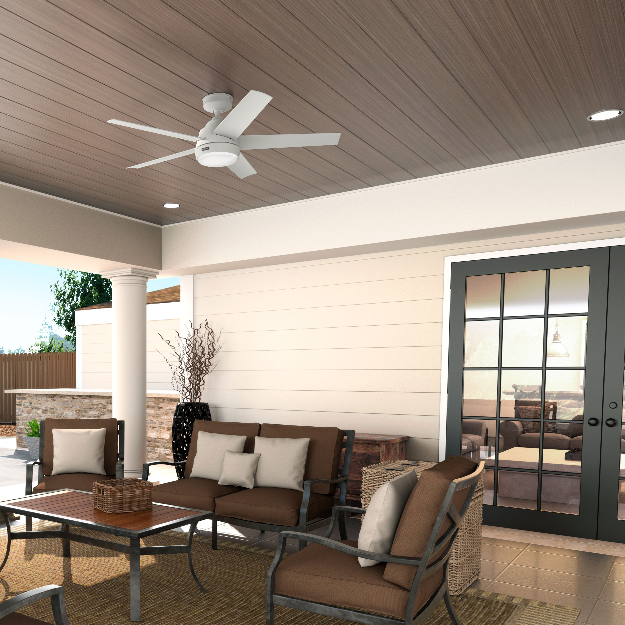 Terrasse mit Möbeln. Deckenventilator, Stühle, Sofa und Tisch auf einem Teppich. Tür führt nach innen. Braun- und Beigetöne.